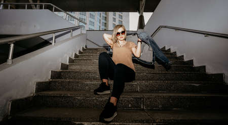 Blonde in sunglasses is wearing a denim jacket sitting on the steps. Modern girlの写真素材