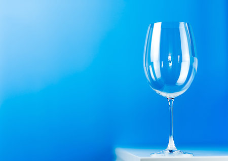 Empty wine glass on a blue background stands on a white table
