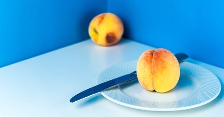 Ripe peach on a white plate with a knife on a blue background. Corner table