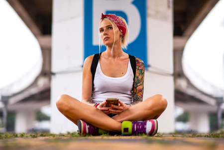 Modern girl sitting on a road marking. Carries a yellow backpack. Tattooed handsの写真素材