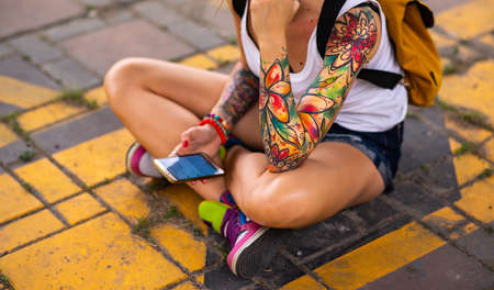 Modern girl sitting on a road marking. Carries a yellow backpack. Tattooed handsの写真素材