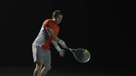 Man hitting tennis ball with racket, isolated on blackの写真素材
