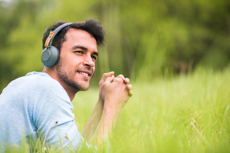 Beautiful young man listen the music with headphones, relax on the green grassの写真素材