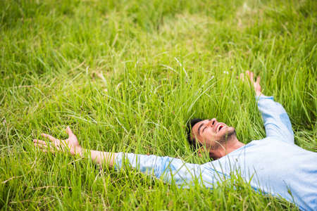 Happy pretty man lying on the green grass with arms outstretchedの写真素材