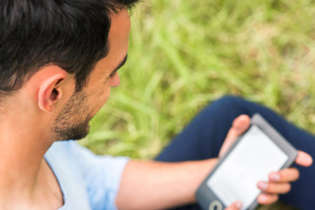 Smiling and happy business man working on device and sitting on the green grass