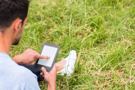 Cropped shot of a young business man working on device and sitting on the green grassの写真素材