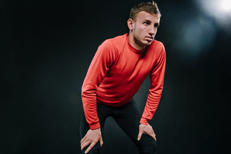 Attractive thoughtful man athlete relaxing after hard workout at the gym, put his hand on the legs...