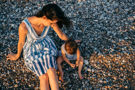 Top view of beautiful brunette woman play with daughter on the beach background. Happy family in...
