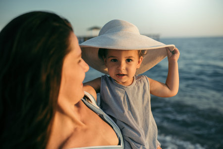 Beautiful portrait of mother and daughter play with hat on the sea and beach background. Happy...