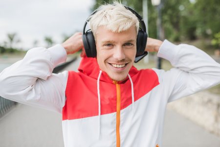 Smiling attractive blond hipster guy listening to contemporary music using his headphones walking in...