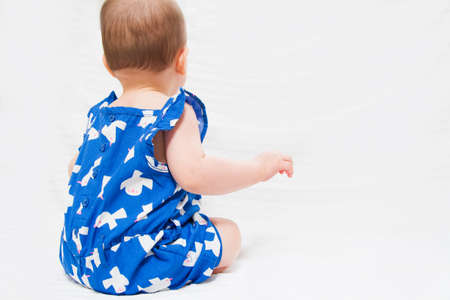Adorable baby sitting on white background with backの写真素材