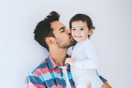 Attractive close up portrait of hipster father kissing his little daughter. Young dad is enjoying time with his child. Handsome father with little girl. Happy father and daughter. Lifestyle family.の写真素材
