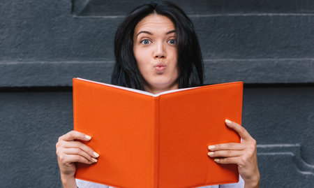 Beautiful and funny female student holds book, has shocked expression as tomorrow is exam, on black...