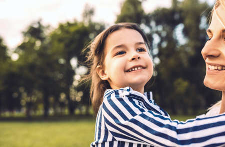 Beautiful happy little girl daughter embracing her mother in the park. Loving smiling mother and daughter spend time together in the park. Happy motherhood time. People and emotionの写真素材