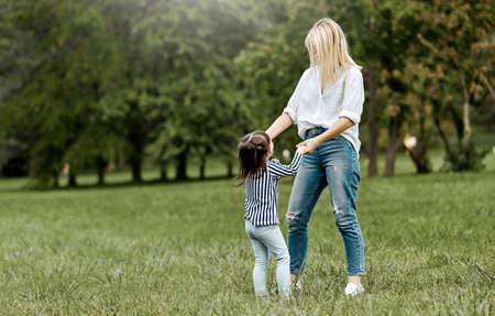 Outdoors image of cute happy little girl playing with her beautiful mother in the park. Happy family time together. Positive emotion. Good relationship between mom and daughter. Mother's day conceptの写真素材