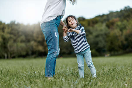 Image of cute happy little girl playing with her beautiful mother outdoors in the park. Happy family time together. Positive emotion. Good relationship between mom and daughter. Mother's day conceptの写真素材