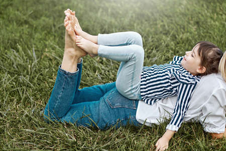 Horizontal side view of beautiful woman lying and playing with her cute little girl on the green grass outdoors. Happy child and mother spend time together in the park. Mother's day conceptの写真素材