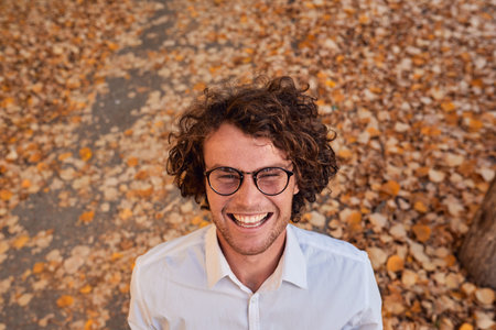 Outdoor autumn shot of smiling handsome young businessman with glasses outdoors. Male student posing against yellow leaves. Smart guy in white shirt and spectacles with curly hair on street.Copy spaceの写真素材