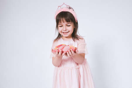 Portrait of cute little girl wearing pink dress in tulle with princess crown on head isolated on white background before blowing confetti. Pretty girl smiling with a lot of confetti for birthday partyの写真素材