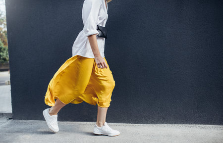 Cropped horizontal image of attractive woman in beautiful yellow skirt runing on the street. Caucasian female fashion model walking over gray wall background outdoor with copy space.の写真素材