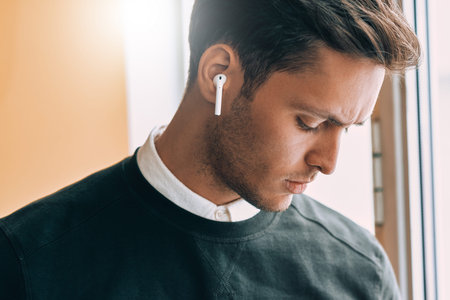 Closeup portrait of sad young handsome man speaking with a friend using wireless earphones. Serious...