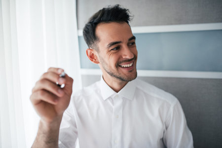 Happy and smiling handsome businessman showing or poiting something with a pen and looking at one...