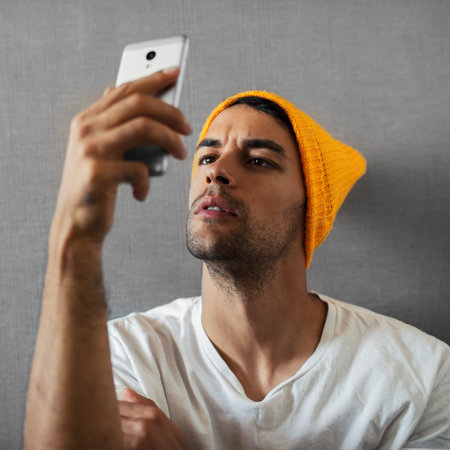Attractive, handsome and serious young man , reading someting, taking selfie. Wearing orange hat and...