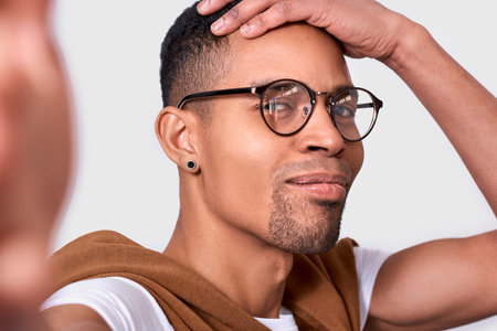 Closeup image of happy handsome African American young man smiling, wearing eyewear, looking at the camera and taking self portrait. Cheerful male posing in studio background. People and emotionの写真素材