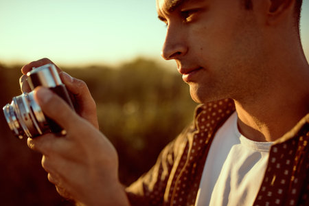 Amazing close up portrait of handsome young man with vintage camera,on a meadow background. Travel...