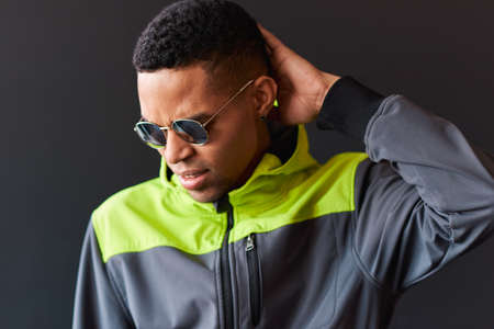 Young African American man wearing round mirror sunglasses touching his head and frowning his face, looking down, posing over black studio background. Thoughtful male thinking about somethingの写真素材