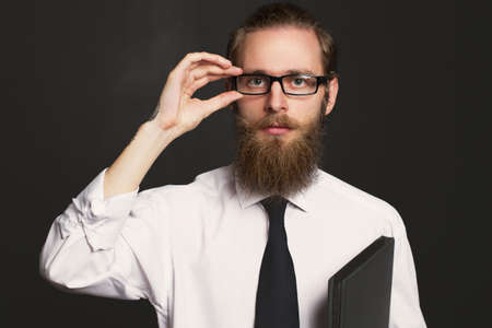 Portrait of serious hipster bearded businessman with documents. Boss in glasses posing in business suit on black background.の写真素材