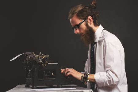 Handsome young hipster businessman thinking and writing with vintage typewriter. Old fashion style.の写真素材