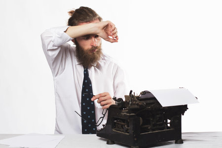 Handsome young hipster businessman thinking and writing with vintage typewriter. Old fashion style.