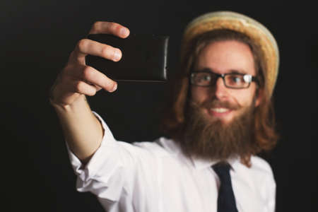 Hipster businessman with glasses and hat taking self portraits with his smartphoneの写真素材