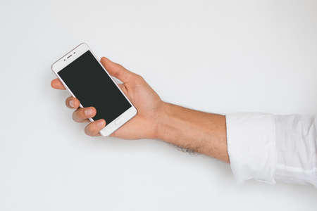 Hand of a man holding mobile smart phone with black display isolated on light gray background. Presentation of a innovation device of technology. Commercial modern presentation concept.の写真素材