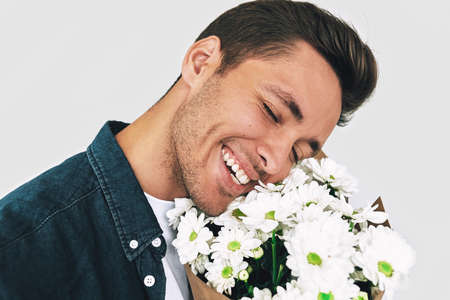 Closeup portrait of young handsome man smiling with closed eyes enjoy the smell of white flowers. Happy male with a bunch of flowers, isolated on white background. Valentine's Day. Mother's Dayの写真素材