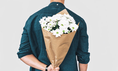Rear view of young man smiling and delivering a bouquet of white flowers. Attractive male model with...
