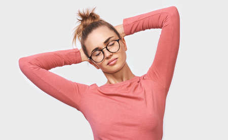 European joyful young woman holding arms on head while enjoy the free time with closed eyes, standing over white studio background. Positive people emotions concept.の写真素材
