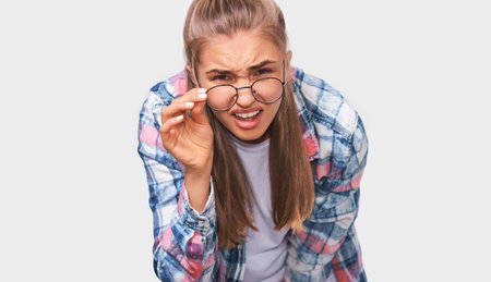 Close up portrait of displeased and questioned young woman taking off her transparent eyewear,...