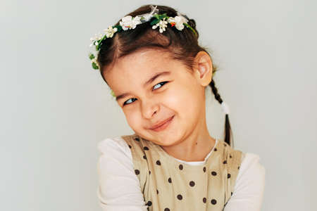 Funny little girl adorable hairstyle with flowers, smiling brightfully, looking to the camera with happy expression. Toddler beautiful girl posing on light grey studio wall. People, emotion and familyの写真素材