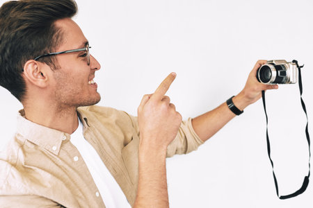 Cheerful freelancer man taking selfie over white studio background. Young male smiling and wearing eyewear making self portrait and blogging using digital camera.の写真素材