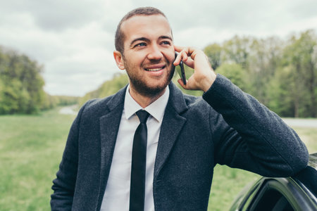 Attractive European caucasian manager in stylish formal coat using mobile phone, near to his car...