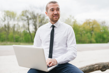 Casual businessman wearing white shirt, typing on his computer making report of his firm using...