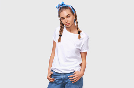 Charming beautiful young woman wearing white t-shirt, blue headband with hands in the pockets,...