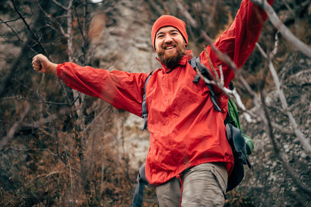 Portrait of happy young hiker man hiking in mountains wearing red clothes exploring new place. Traveler bearded man trekking and mountaineering during his journey. Travel, people, sport and lifestyleの写真素材