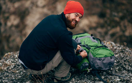 Rear view image of young hiker man relaxing in mountains after hiking. Outdoors shot of traveler male in red hat, sitting alone on rock, have a break after mountaineering. Travel and lifestyle conceptの写真素材