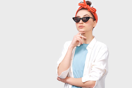 Beautiful serious brunette young woman wears black sunglasses, white shirt and trendy red headband,...