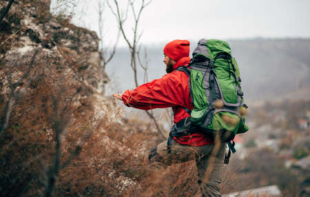 Rear view of young hiker man hiking in mountains dressed in red clothes exploring new places. Traveler bearded male trekking and mountaineering during his journey. Travel, people, sport, lifestyleの写真素材