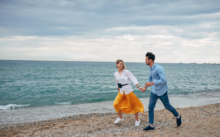 Horizontal outdoor shot of happy smiling young couple walking on beach. Young handsome man and...