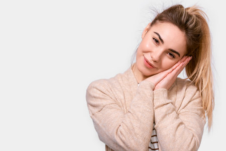 Kind young woman in beige sweater and ponytail, smiling with pleasant expression, looking to the...